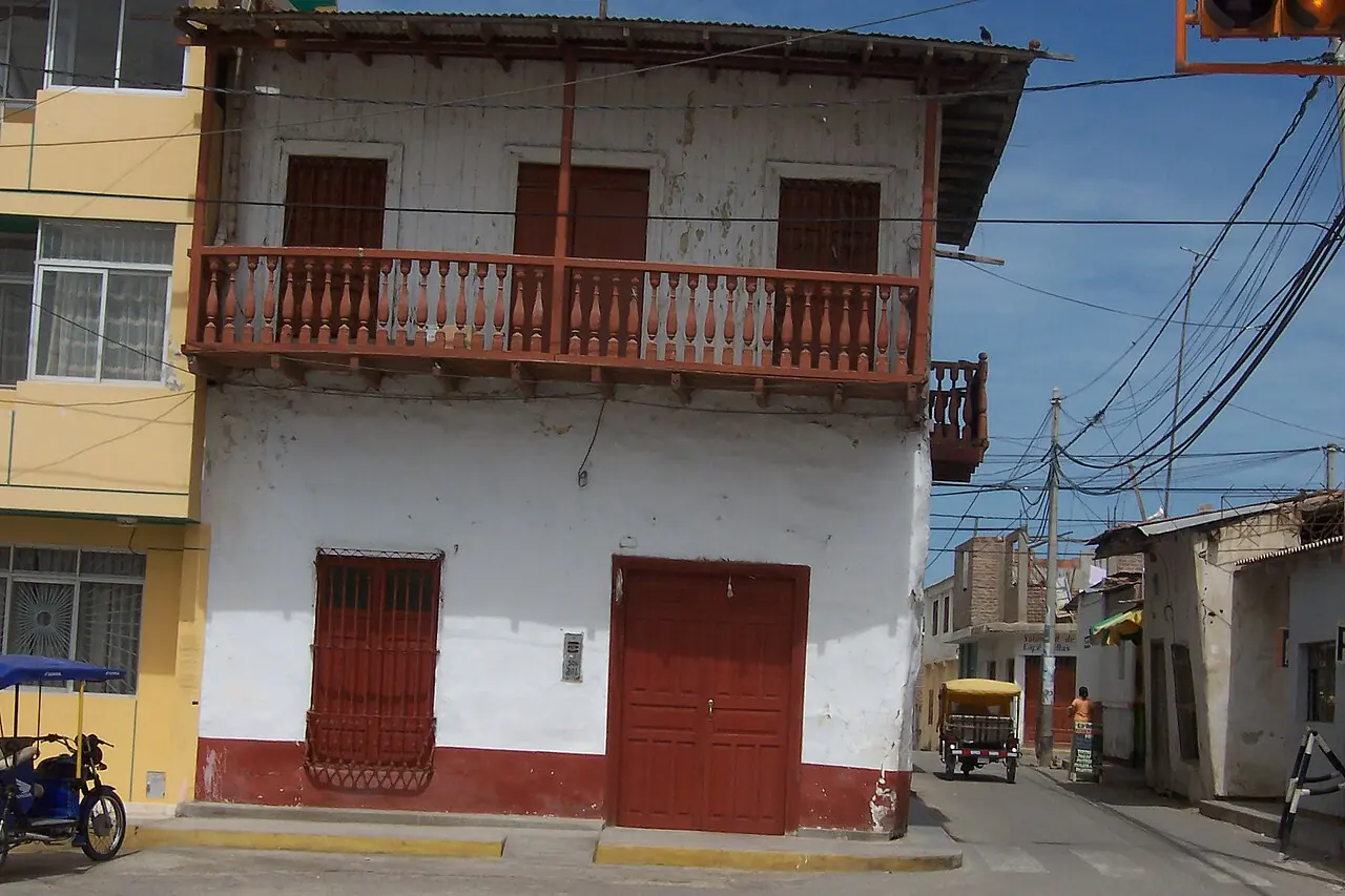 Casona de dos pisos con balcón de madera y portones rojos en una esquina de la Plaza de Armas de Sechura