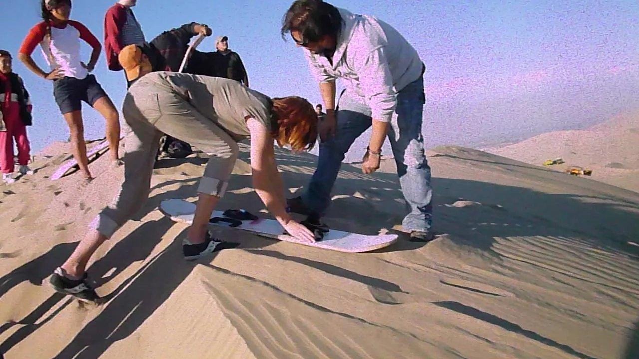 Turistas preparando su tabla para deslizarse en una duna de arena clara