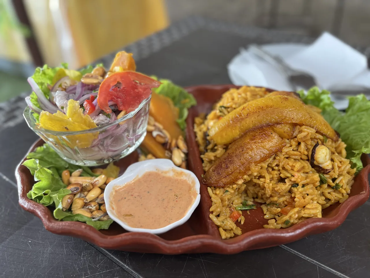 Plato de barro con ceviche en copa, cancha y camote, y arroz con mariscos con plátano frito