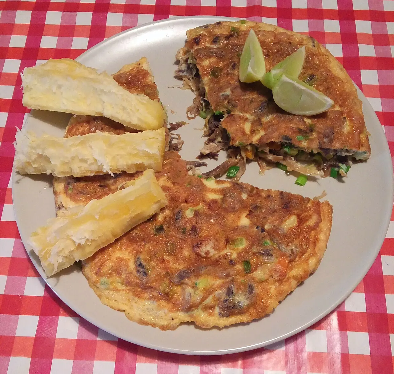 Tortilla de raya dorada con yuca y limón sobre un mantel a cuadros rojos